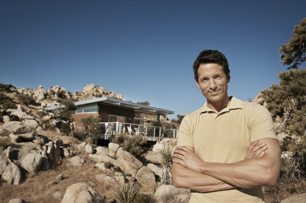 A man standing in front of an eco home in the hills