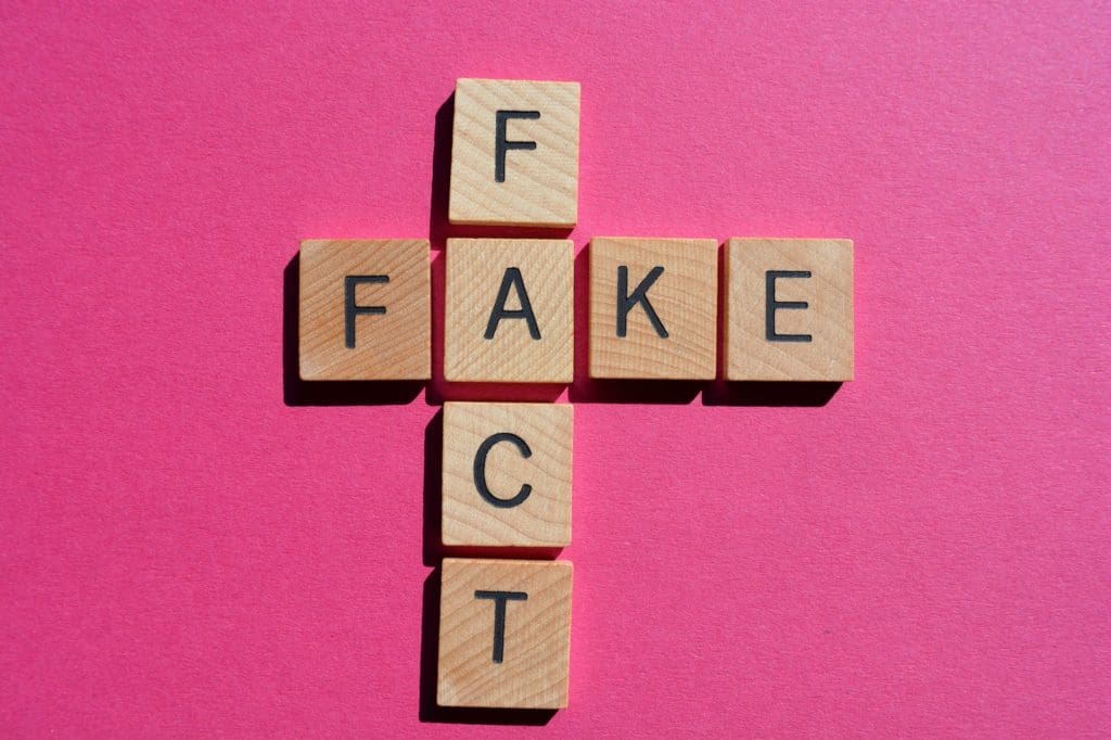 Fact, Fake. Words in 3D wooden alphabet letters in crossword form on bright pink background